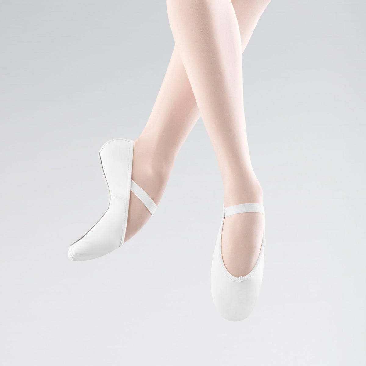 White ballet shoes worn with sheer white stockings on a light gray background