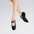 Black ballet shoes worn by a person on a light gray background