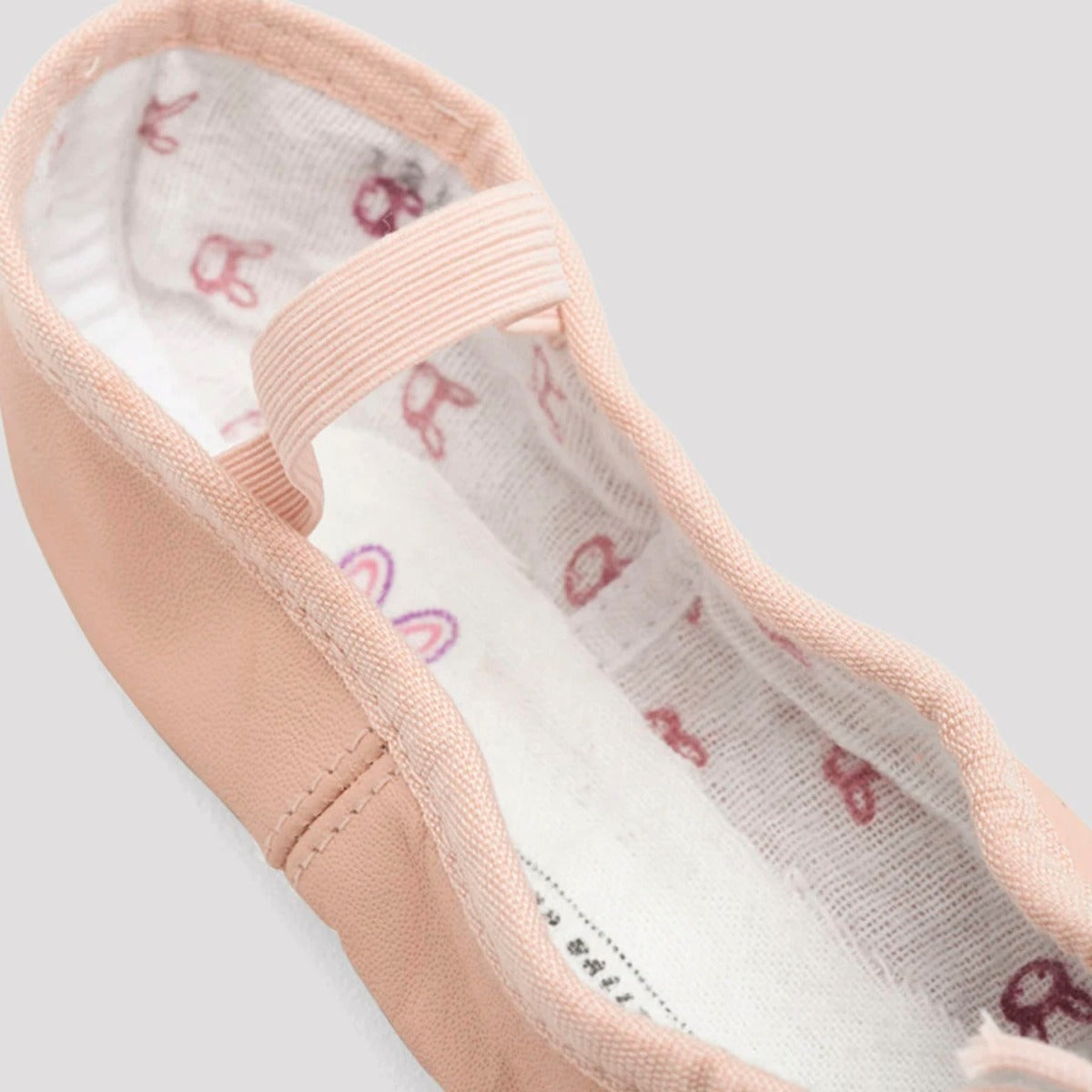 Close-up of a pink ballet shoe with white lining featuring red and pink floral patterns on a light gray background.