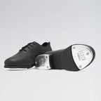 Black tap dance shoe with metallic toe on a light gray background
