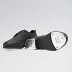 Black tap dance shoe with metallic toe on a light gray background