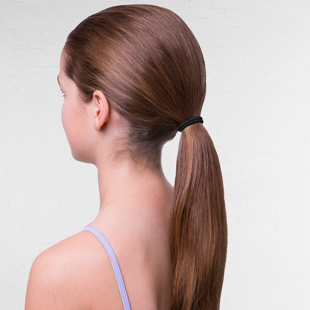 Woman with long brown hair tied into a ponytail against a light gray background