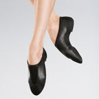 Black leather ballet shoes worn by a person on a gray background