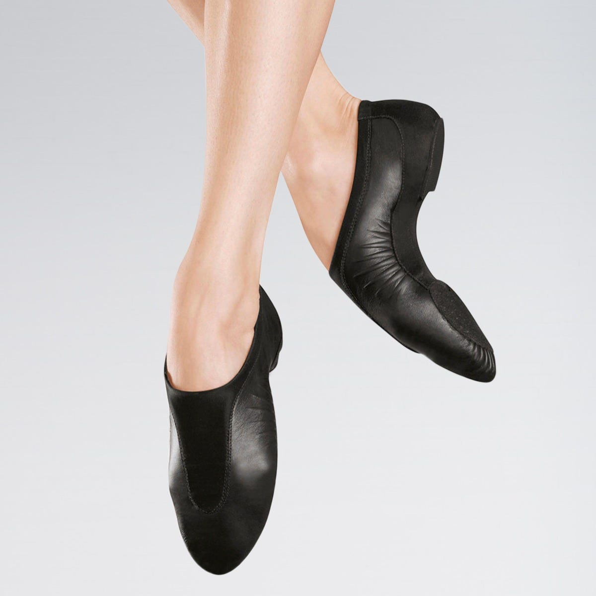 Black leather ballet shoes worn by a person on a gray background
