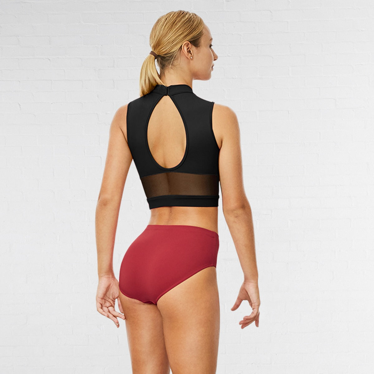 Woman wearing a black crop top and red high-waisted bikini bottom on a white background