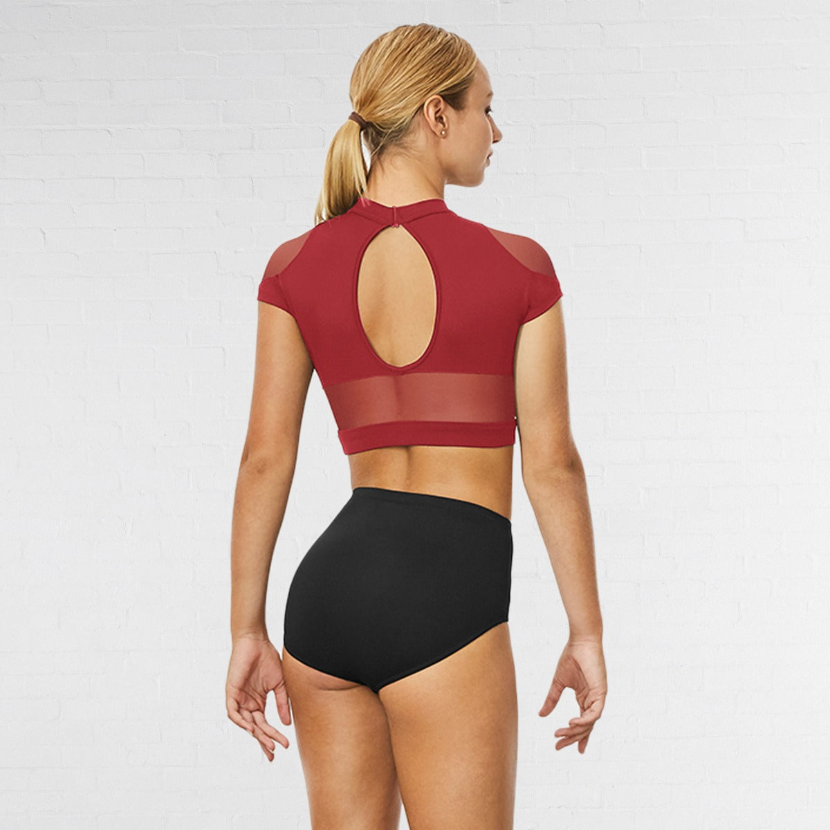 Woman wearing a red mesh top and black high-waisted bottoms on a white background
