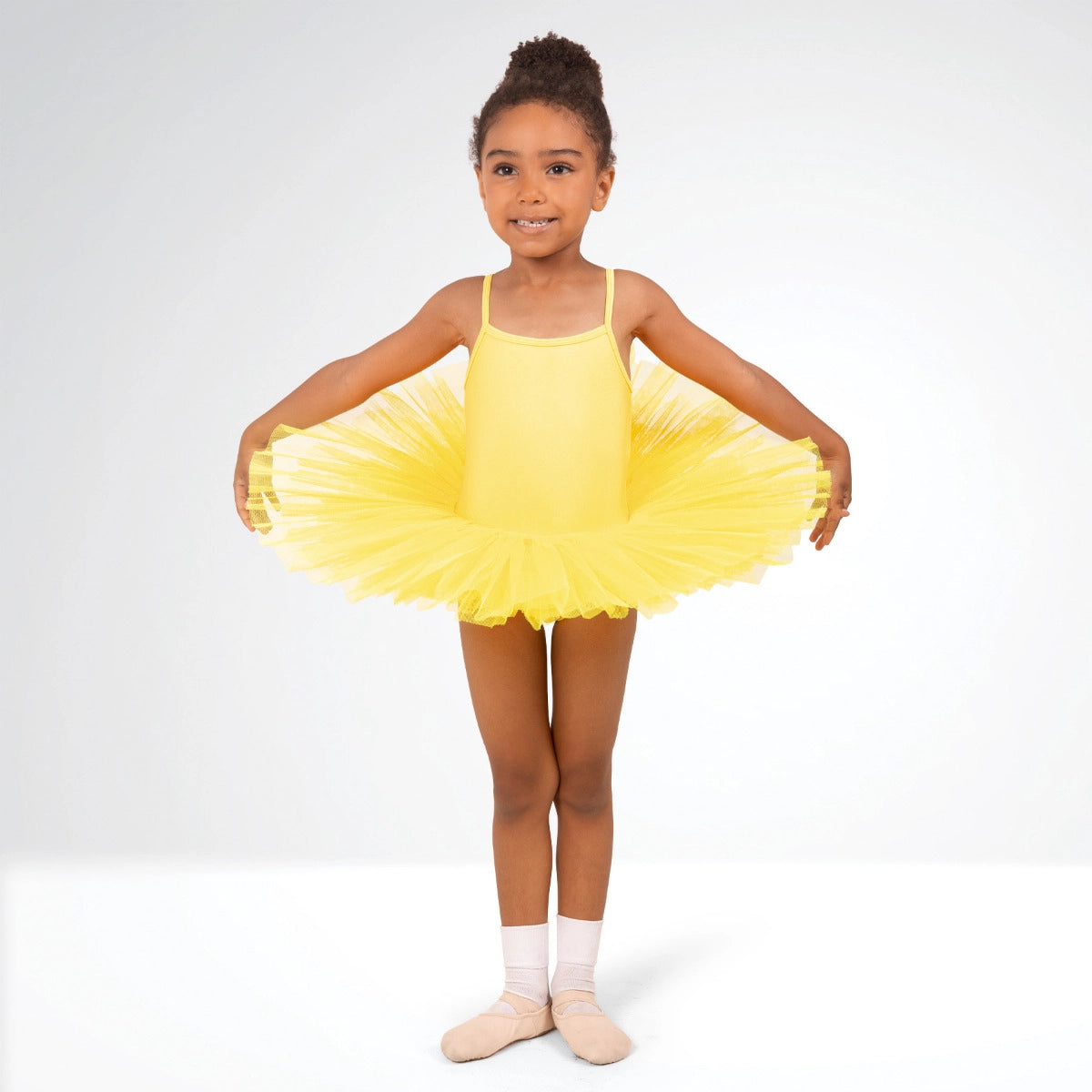 Young girl in a yellow tutu dress posing against a white background