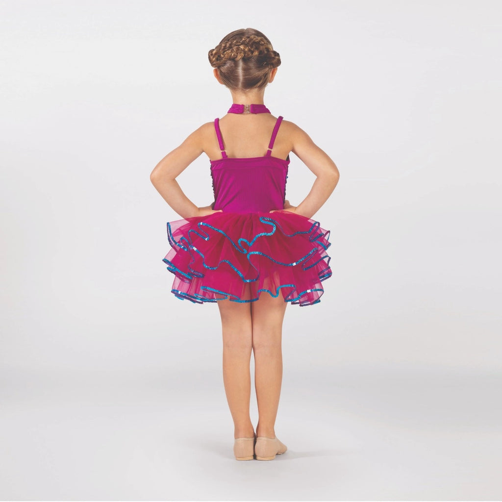 Young dancer wearing a raspberry pink sequin tutu costume by 1st Position featuring a crossover halterneck design, sparkling sequin bodice and layered tutu skirt with blue glitter trim.