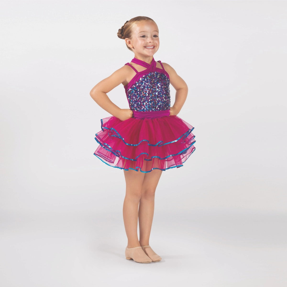 Young dancer wearing a raspberry pink sequin tutu costume by 1st Position featuring a crossover halterneck design, sparkling sequin bodice and layered tutu skirt with blue glitter trim.