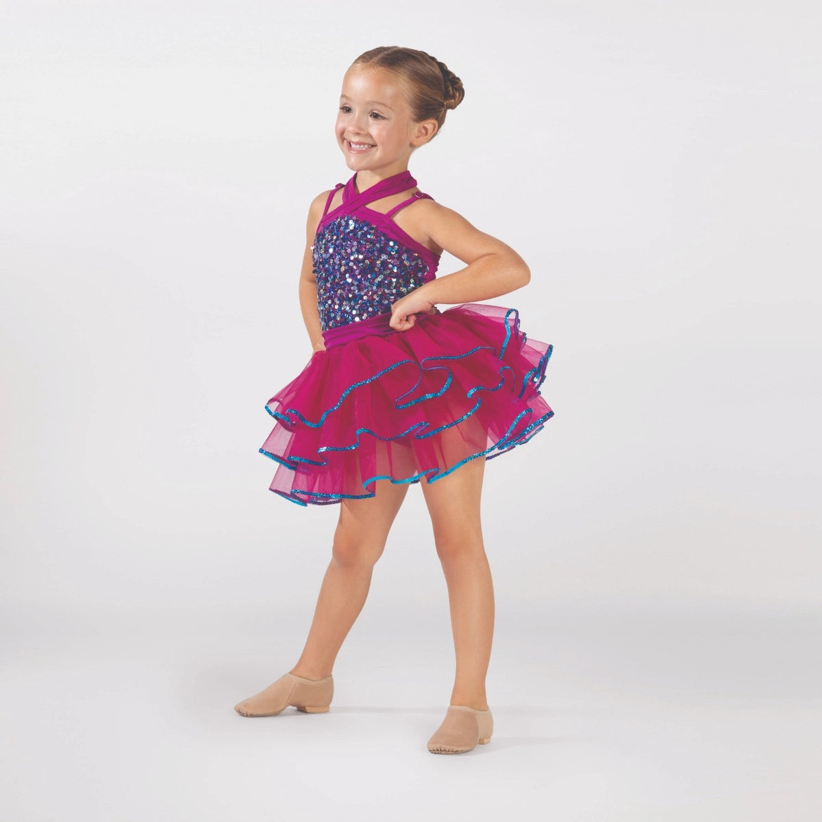 Young dancer wearing a raspberry pink sequin tutu costume by 1st Position featuring a crossover halterneck design, sparkling sequin bodice and layered tutu skirt with blue glitter trim.