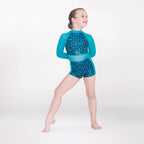 A young girl modeling a two-piece leotard swimsuit with a teal and blue patterned design, standing against a plain white studio background.