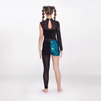 A child model shown from the back wearing a black long-sleeve leotard with a sheer mesh back panel and black tights, paired with teal patterned shorts, against a plain light gray studio background.