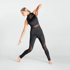 A woman in a black sleeveless mesh-paneled activewear set with matching leggings poses dynamically against a light gray studio background.