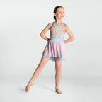 A young girl dancer posing in a sleeveless halter-neck leotard dress with a multicolor floral patterned bodice, a light blue waistband, and a layered pink and light blue mesh skirt, set against a plain light gray studio background.