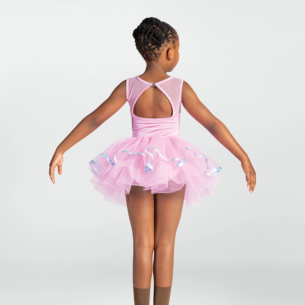 A young girl viewed from behind wearing a light pink ballet leotard with a ruffled tulle skirt and blue ribbon accents, posed against a light gray studio background.