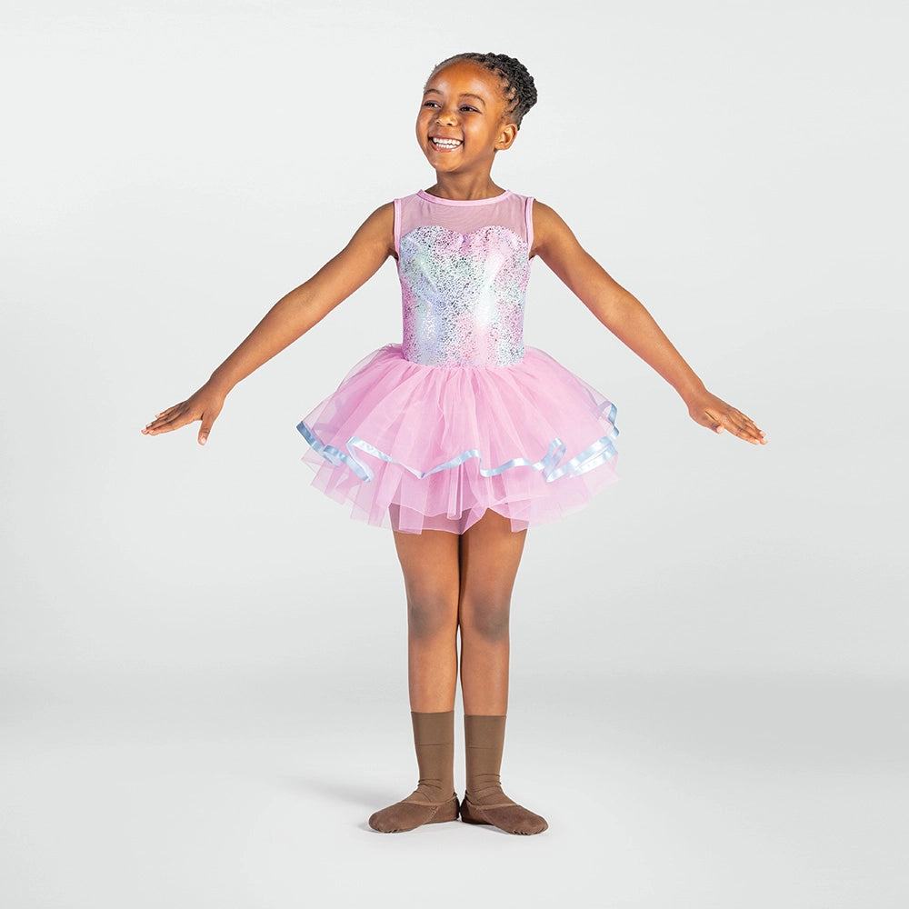 A young girl wearing a pink sequined ballet tutu dress with a sheer bodice, standing in ballet slippers against a light gray studio background.