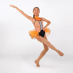 A young girl dancer posing in a sleeveless orange and black leotard with a sheer orange tutu skirt, set against a plain light gray studio background.