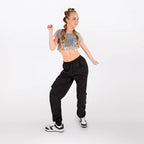 A young woman posing in a sparkly silver short-sleeve crop top and black cargo pants against a plain white studio background.