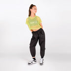 A woman modeling a neon yellow-green cropped mesh top and black cargo jogger pants against a plain white studio background.