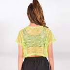 A woman viewed from the back wearing a neon yellow-green short-sleeve mesh crop top over a dark green top and black pants, against a light gray studio background.