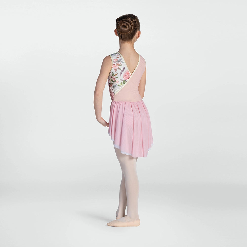A young girl dancer is shown from the back wearing a sleeveless pink leotard with a floral patterned back panel, a pink pleated skirt, and light pink tights against a light gray studio background.