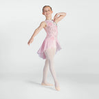 A young ballerina girl posing in a light pink sleeveless leotard with a floral pattern, sheer pink tutu skirt, and light pink tights against a light gray studio background.