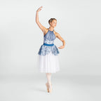 A female ballet dancer posing in a sleeveless blue and white patterned leotard with a white tulle skirt, standing en pointe against a light gray studio background.