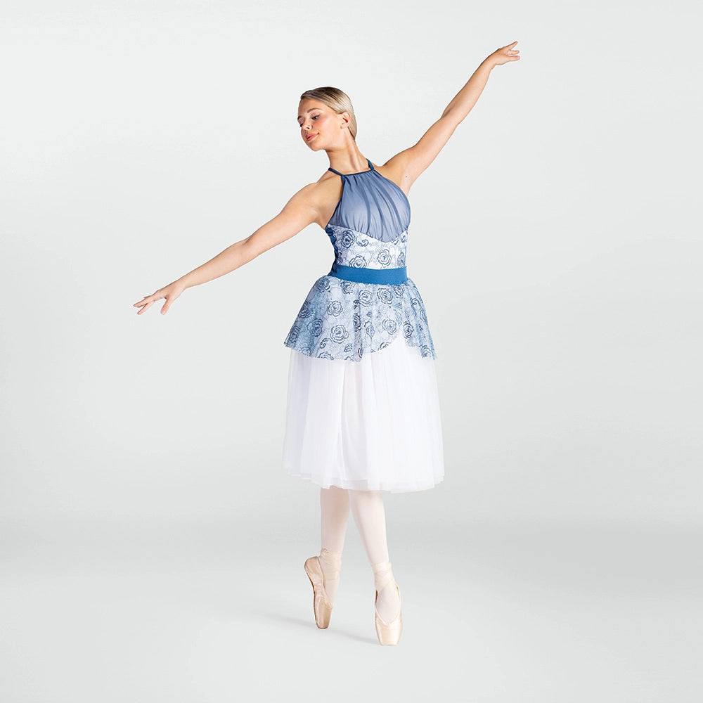 A woman in a blue and white ballet leotard and tulle skirt poses in a ballet position on pointe against a light gray studio background.