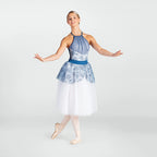 A female dancer posing in a blue and white patterned halter-neck tutu dress with a white tulle skirt, standing on pointe in ballet slippers against a light gray studio background.
