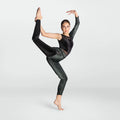 A female dancer posing in a black long-sleeve leotard with sheer mesh panels and black-to-silver glittery leggings, set against a plain light gray studio background.