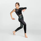 A woman modeling a black two-piece dancewear set consisting of a long-sleeve crop top with sheer mesh shoulders and high-waisted leggings with a textured black-and-white pattern, set against a light gray studio background.