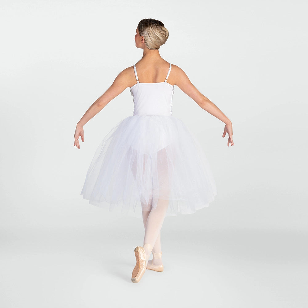 A young ballerina viewed from behind, wearing a white spaghetti-strap tutu dress with a full tulle skirt and pink pointe shoes, posed against a light gray studio background.