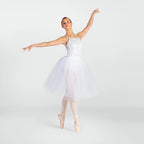 A ballerina posing in a white sleeveless tutu dress with a lace bodice and a full tulle skirt, on pointe in a light pink pointe shoe against a light gray studio background.