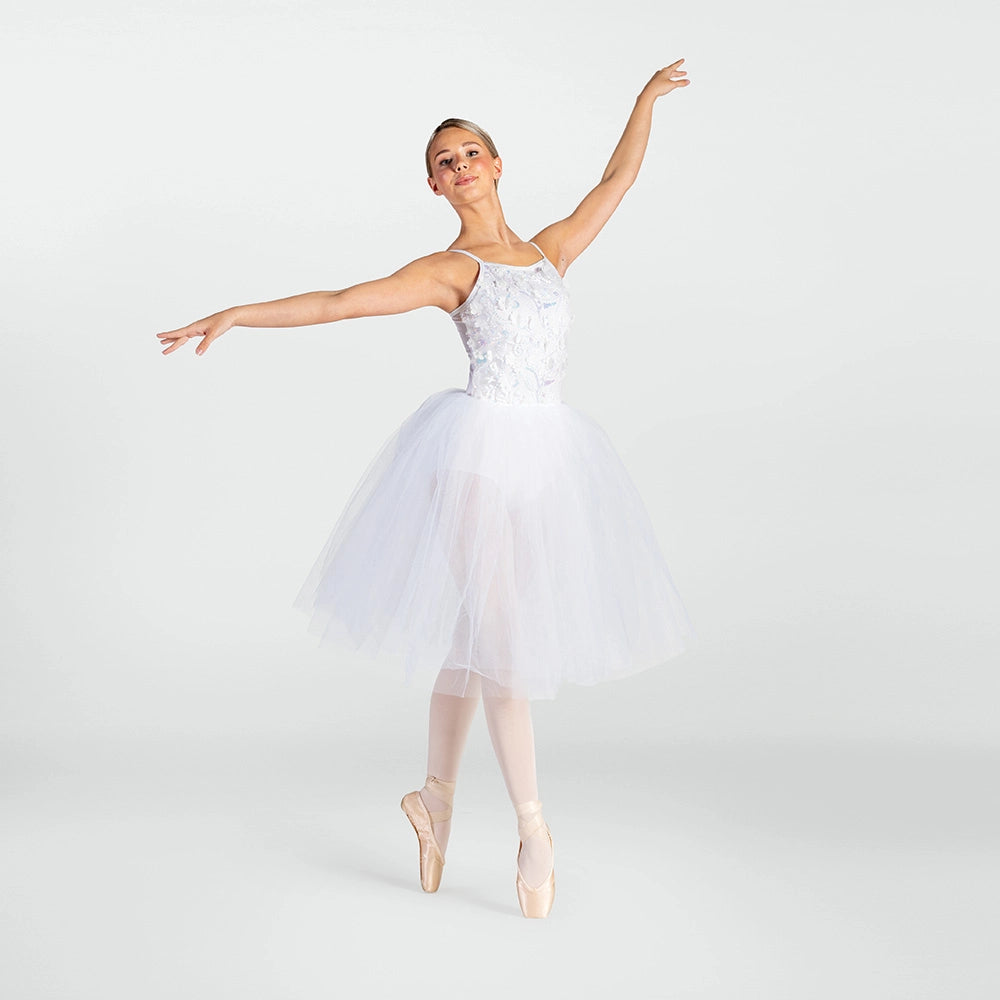 A ballerina posing in a white sleeveless tutu dress with a lace bodice and a full tulle skirt, on pointe in a light pink pointe shoe against a light gray studio background.