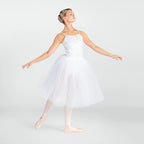A woman posing as a ballerina in a white lace and tulle tutu dress with pink pointe shoes against a light gray studio background.