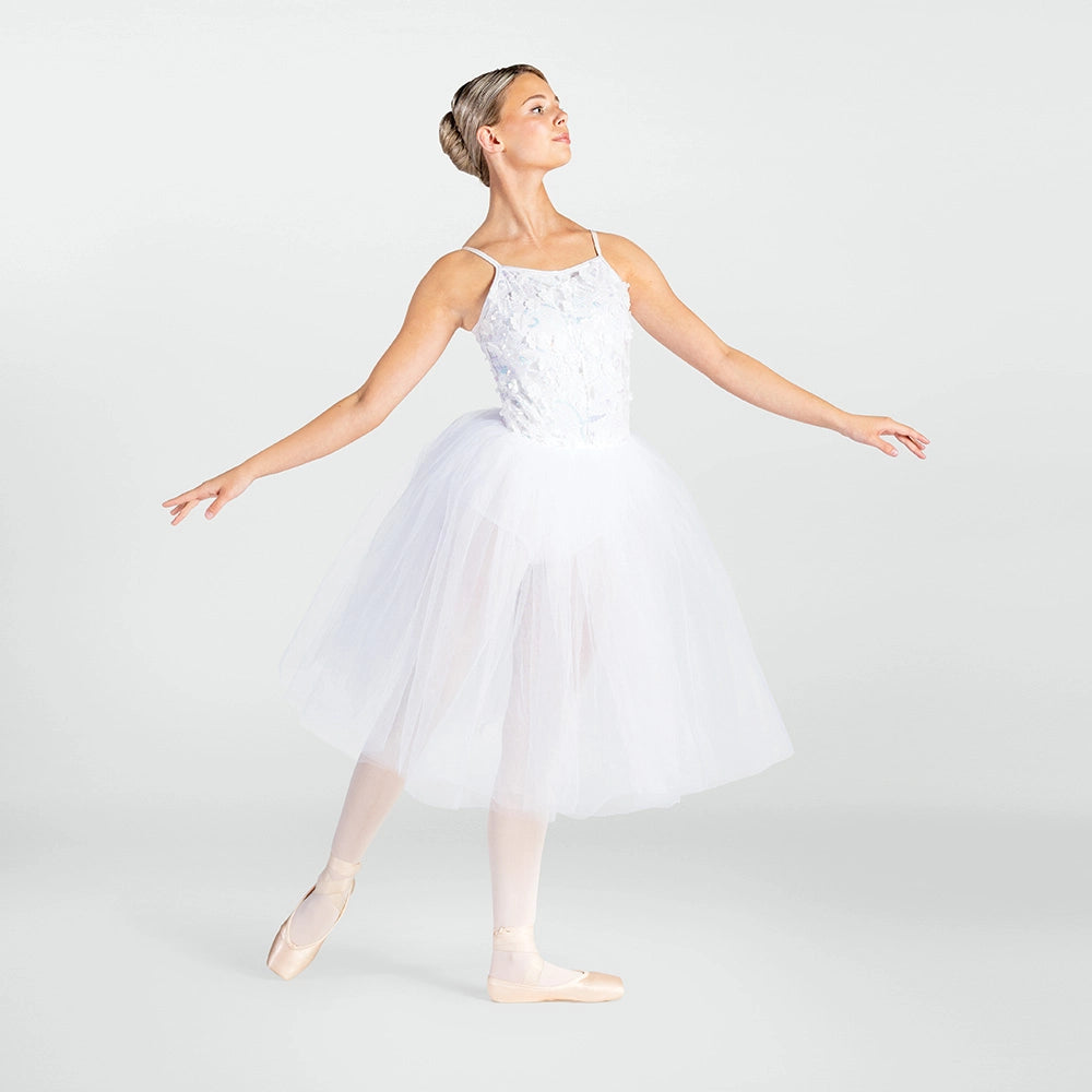 A woman posing as a ballerina in a white lace and tulle tutu dress with pink pointe shoes against a light gray studio background.