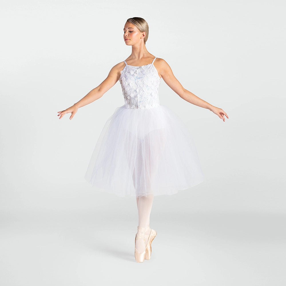 A woman in a white ballet tutu dress with a lace bodice and tulle skirt, posed en pointe on a light gray studio background.
