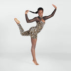 A young dancer posing in a leopard print bodysuit with sheer black long sleeves, set against a plain light gray studio background.
