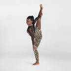 A young girl in a leopard print leotard and sheer black long-sleeve top poses in a full side stretch against a light gray studio background.