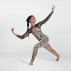 A woman posing in a leopard print bodysuit with sheer black long sleeves, set against a plain light gray studio background.