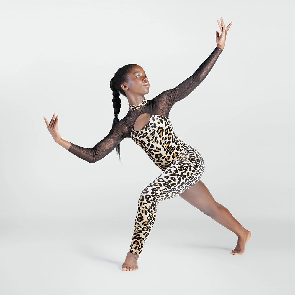 A woman posing in a leopard print bodysuit with sheer black long sleeves, set against a plain light gray studio background.