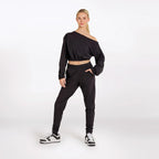 Woman wearing a black off-shoulder top and black jogger pants on a white background