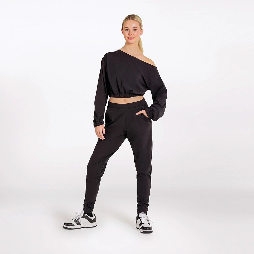 Woman wearing a black off-shoulder top and black jogger pants on a white background