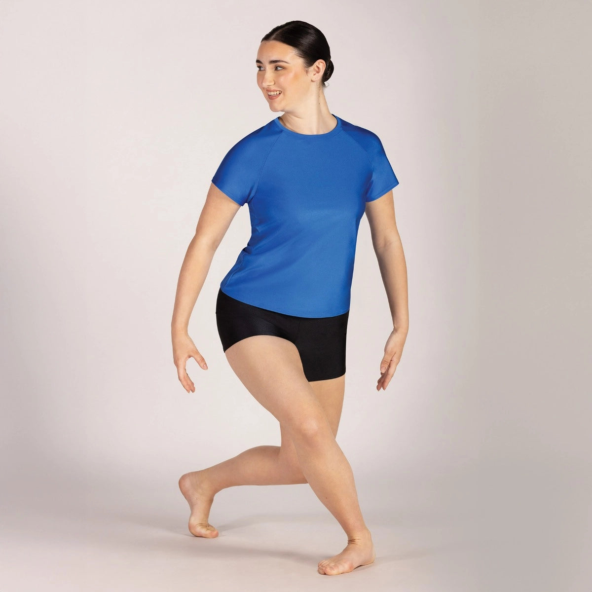 Woman wearing a blue athletic shirt and black shorts on a plain background