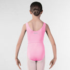 A young girl viewed from behind wearing a bright pink sleeveless dance leotard with a small silver 'RAD DANCE' logo on the upper back, paired with light pink tights, standing against a white brick wall.