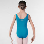 A young girl viewed from behind wearing a bright turquoise blue sleeveless dance leotard with 'rad Dance' printed in white on the upper back, paired with light pink tights, standing against a white brick wall.